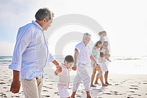 Three generation family on vacation holding hands while walking along the beach together. Mixed race family with two