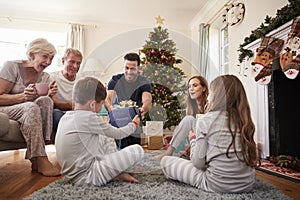 Three Generation Family Wearing Pajamas In Lounge At Home Opening Gifts On Christmas Day