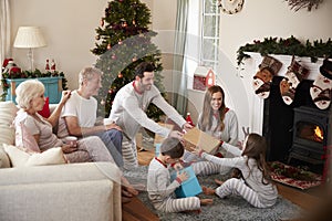 Three Generation Family Wearing Pajamas In Lounge At Home Opening Gifts On Christmas Day