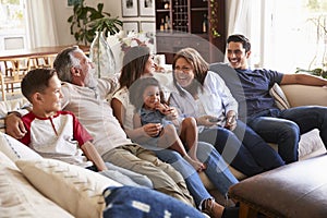 Three generation Hispanic family sitting on the sofa watching TV, grandmother using remote control