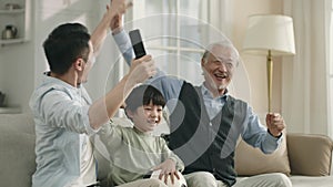 three generation soccer fans cheering while watching game on tv