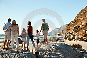 Three generation white family on a beach stand holding hands, admiring view, full length, back view