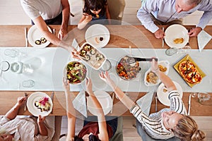 Three generation white family sitting at a dinner table together serving a meal, overhead view