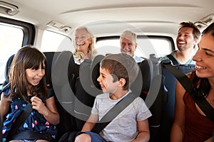 Three generation white family sitting in two rows of passenger seats in a car, looking at each other