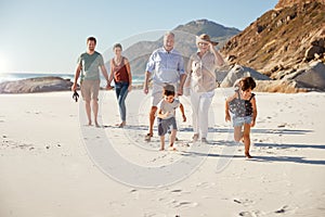 Three generation white family walking together on a sunny beach, kids running ahead