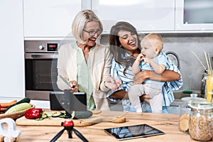 Three Generations Family. Grandma, mother and baby record a cooking vlog or podcast while chopping vegetables for a healthy