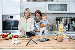 Three Generations Family. Grandma, mother and baby record a cooking vlog or podcast while chopping vegetables for a healthy