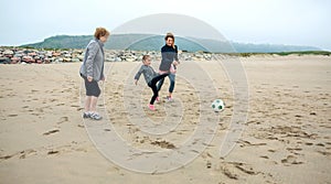 Three generations female playing soccer on the beach