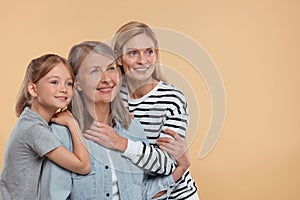 Three generations. Happy grandmother, her daughter and granddaughter on beige background, space for text