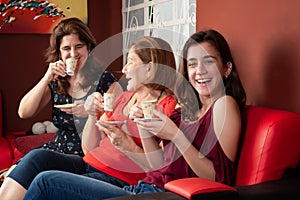 Three generations of hispanic women laughing and drinking coffee