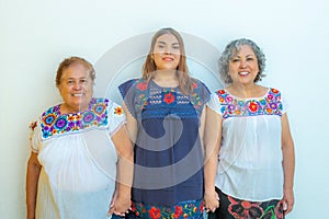 Three generations of latin Mexican women smiling, grandmother, granddaughter and daughter with floral printed blouses holding hand