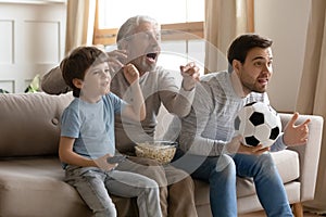 Three generations of men watch football match at home