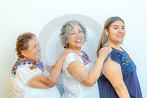 Three generations of smiling Mexican women in a row holding their shoulders