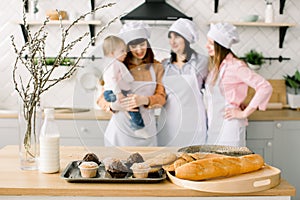 Three generations of women are cooking in the kitchen, focus on the table with maffines and cookies. Homemade food and