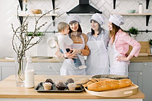 Three generations of women are cooking in the kitchen, focus on the table with maffines and cookies. Homemade food and