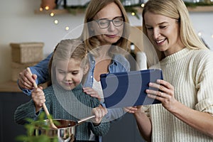 Three generations of women in the kitchen cooking with a tablet