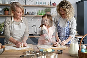Three generations of women kneading dough in kitchen
