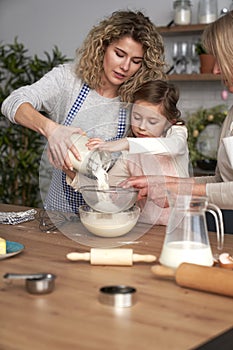Three generations of women sifting flour for homemade cookies