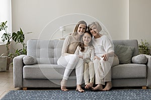 Three generations of women sit on sofa looking at camera