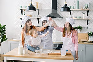 Three generations of women in white aprons are making pizza dough in the kitchen to Mothers Day