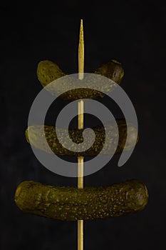 Three gherkins on a skewer, on a dark background