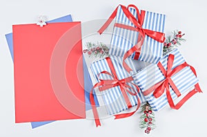 Three gift boxes in a blue stripe with red ribbons, fir branches and a blank sheet of paper lie on a white