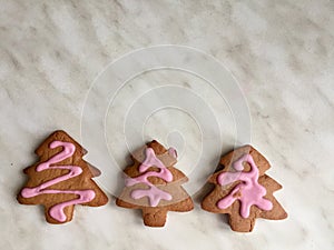 three ginger herringbone-shaped cookies, with pink icing sugar on a grey background