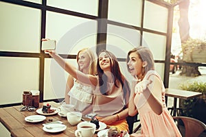 Three girl friends spend time together drinking coffee in the cafe, having breakfast and dessert.