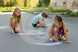 Three girl kids absorbedly drawing chalks on the pavement