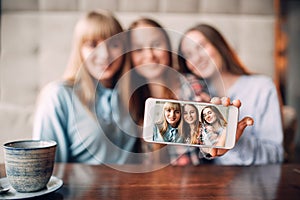 Three girlfriends makes selfie on camera in cafe