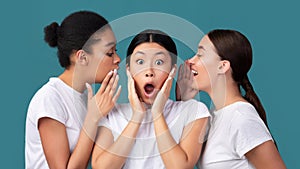 Three Girlfriends Sharing Secrets Standing On Turquoise Background In Studio