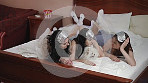 Three girlfriends talking while lying on the bed in the bedroom. Young women with silver sleep masks on their heads are