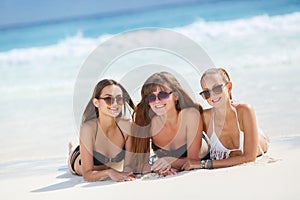 Three girls in bikini sunbathing lying on the sand