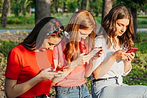 Three girls chatting with their smartphones at the park. Gen Z young girl friends using gadget and having fun outdoors photo