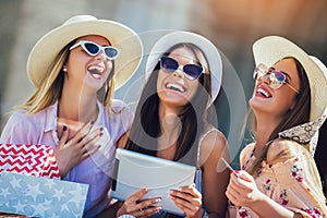 Three girls with colorful shopping bags using digital tablet and credit card