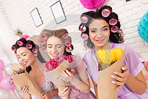 Three girls with curlers in their hair and flowers in hands. They are celebrating women`s day March 8.