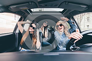 Three girls driving in a convertible car and having fun, listen music and dance