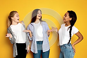 Three Girls Engaging in Lively Conversation Against Vibrant Yellow Background photo