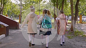 Three girls with flower bouquets walking to school, back view