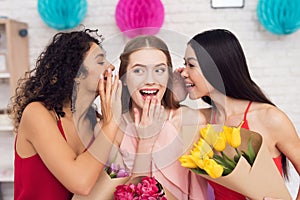 Three girls with flowers gossiping. They are celebrating women`s day March 8.