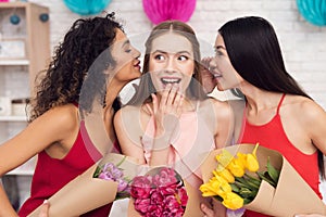 Three girls with flowers gossiping. They are celebrating women`s day March 8.