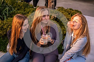 Three girls friends having fun on evening broadway. Eating ice cream, drinking ice fresh milk shake and chewing bubble
