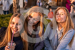 Three girls friends having fun on evening broadway. Eating ice cream, drinking ice fresh milk shake and chewing bubble