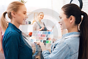 Three girls at garment factory. They are looking at colors for new dress on pattern.