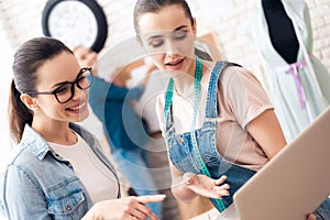 Three girls at garment factory. They are looking for desing for new dress on laptop.