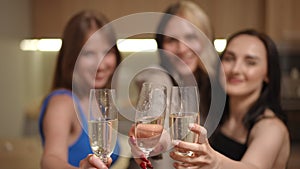 Three girls with glasses of white sparkling wine in their hands, stand in the kitchen in a modern apartment. The girls