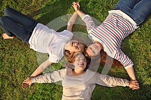 Three girls hold hands and lie on grass