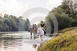 Three girls horseback riding across the river during sunset