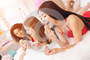 Three girls lying on bed eating cupcakes. They are celebrating women`s day March 8.