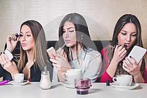 Three girls putting on makeup in a cafe